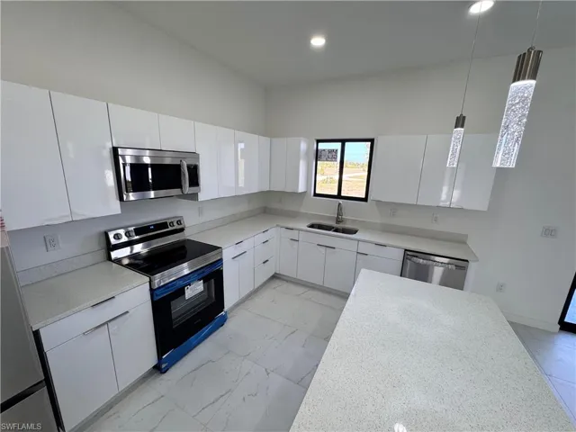 Kitchen with appliances with stainless steel finishes, white cabinets, light marble finish floors, pendant lighting, and modern cabinets