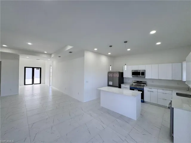 Kitchen featuring white cabinetry, open floor plan, stainless steel appliances, light stone counters, and hanging light fixtures
