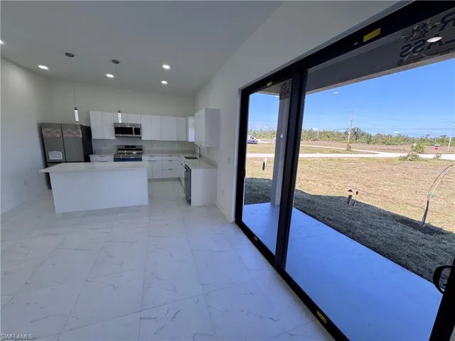 Kitchen with white cabinets, a kitchen island, stainless steel appliances, hanging light fixtures, and light marble finish floors