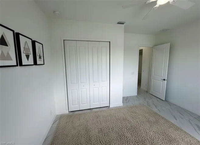 Unfurnished bedroom with light marble finish floors, a ceiling fan, and a closet