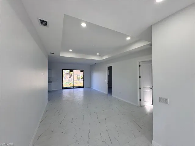 Empty room featuring recessed lighting, light marble finish flooring, and a raised ceiling