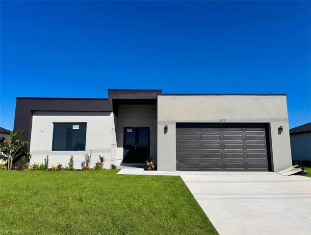 Contemporary house with stucco siding, a garage, a front yard, and concrete driveway