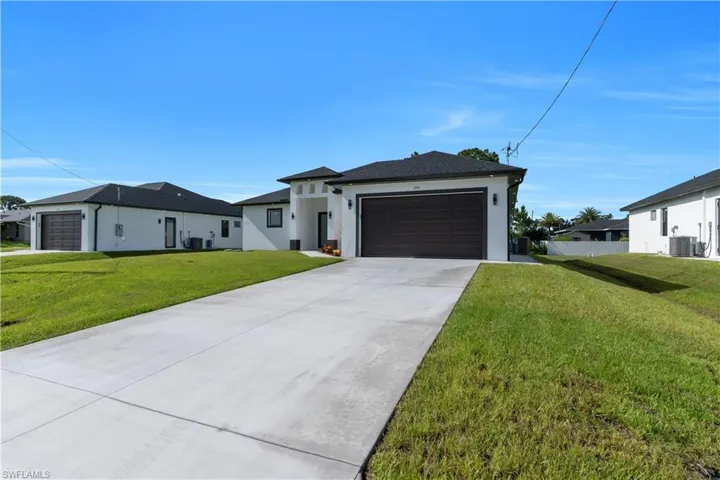 View of front of home with stucco siding, a garage, a front yard, and driveway