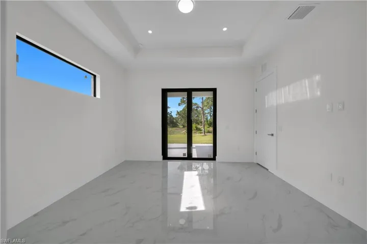 Empty room with marble tiled floors, a raised ceiling, and recessed lighting