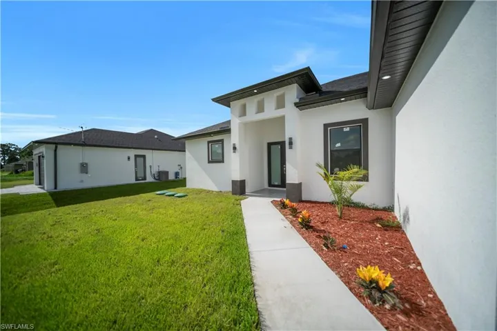 Doorway to property featuring stucco siding, a yard, and a shingled roof