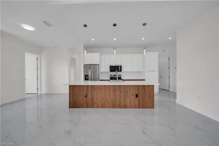 Kitchen with stainless steel appliances, modern cabinets, a large island with sink, light marble finish floors, and recessed lighting