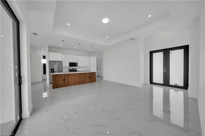 Unfurnished living room featuring a raised ceiling, recessed lighting, french doors, and light marble finish flooring
