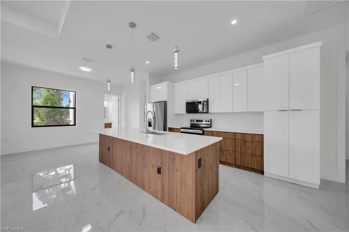 Kitchen featuring appliances with stainless steel finishes, modern cabinets, white cabinets, light marble finish flooring, and a center island with sink