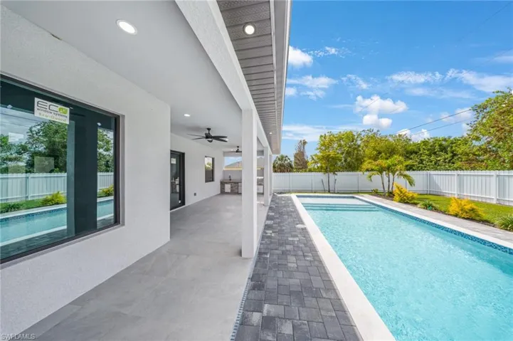 Expansive patio area featuring a rectangular pool, dark paver decking, and a covered outdoor kitchen