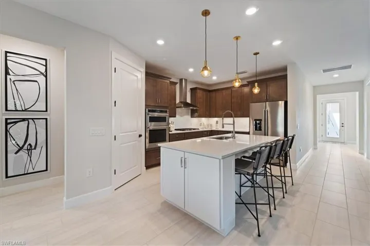 Kitchen with stainless steel appliances, a sink, visible vents, wall chimney exhaust hood, and a kitchen bar