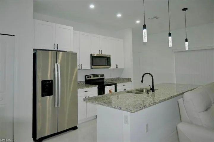 Kitchen featuring stainless steel appliances, light stone counters, decorative light fixtures, white cabinets, and recessed lighting