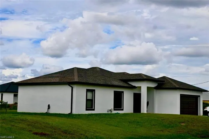 Rear view of house with stucco siding, an attached garage, a lawn, and roof with shingles