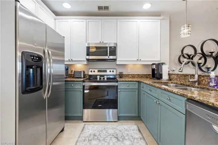 Kitchen with appliances with stainless steel finishes, dark stone countertops, hanging light fixtures, white cabinets, and light tile patterned floors