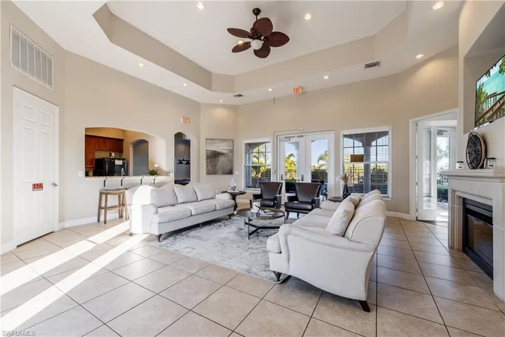 Living room featuring a raised ceiling, a towering ceiling, ceiling fan, light tile patterned floors, and a glass covered fireplace