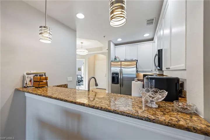 Kitchen featuring appliances with stainless steel finishes, arched walkways, dark stone counters, white cabinets, and pendant lighting