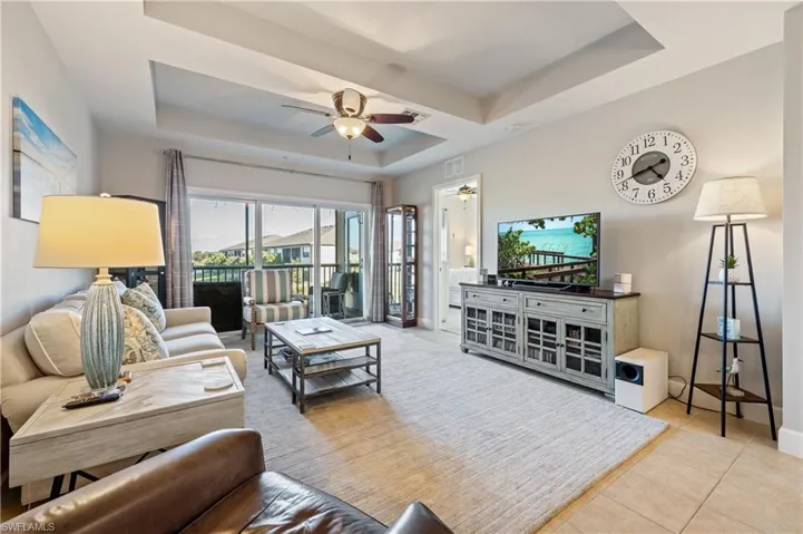 Living area with a raised ceiling, a ceiling fan, and light tile patterned floors