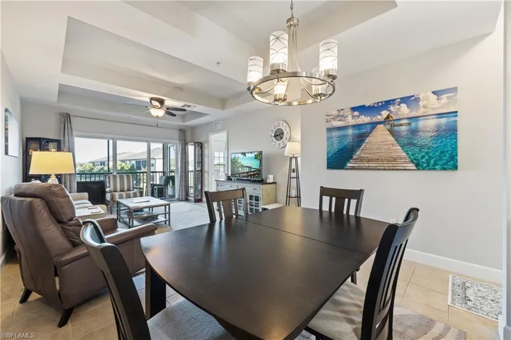 Dining room with a raised ceiling, light tile patterned floors, a chandelier, and ceiling fan