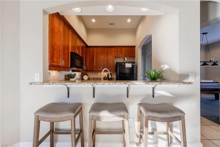 Kitchen with a kitchen breakfast bar, black appliances, light stone countertops, light tile patterned floors, and recessed lighting