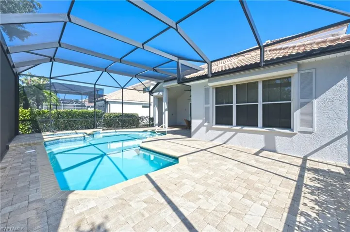Screened-in pool area featuring a rectangular swimming pool with an integrated spa, paver decking, and a stucco exterior with decorative shutters