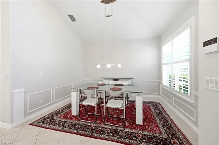 Vaulted ceiling dining area featuring tile flooring, wainscoting, and plantation shutters
