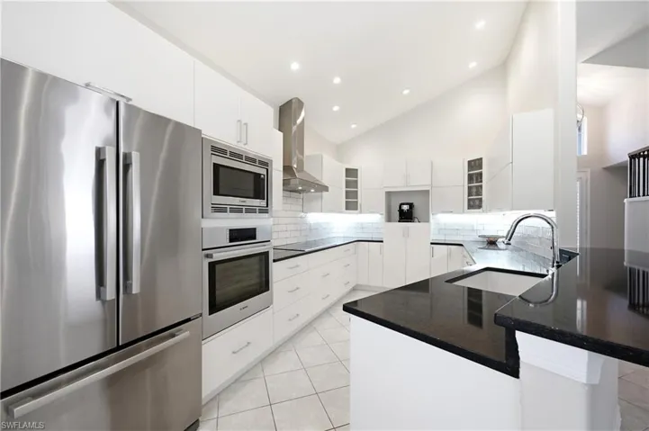 Modern kitchen featuring white cabinetry, dark countertops, integrated stainless steel appliances, a subway tile backsplash, and recessed lighting