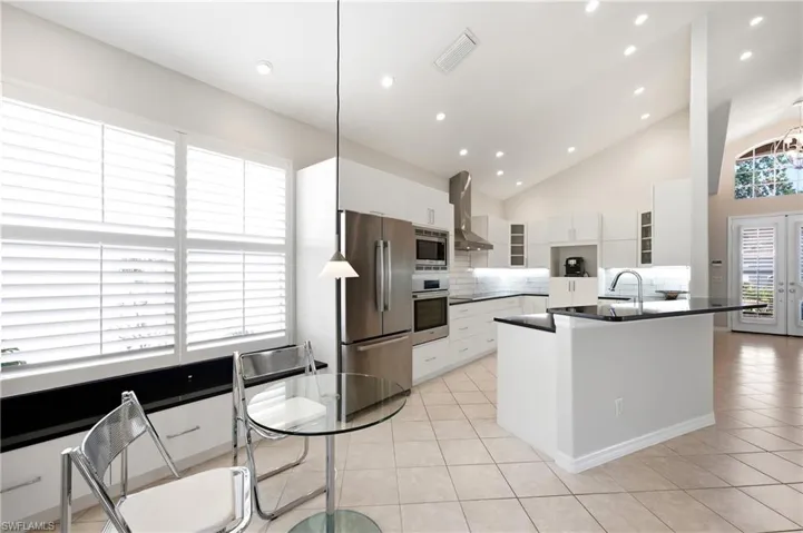 Modern kitchen featuring white cabinetry, stainless steel appliances, and a central island with a sink and dark countertop