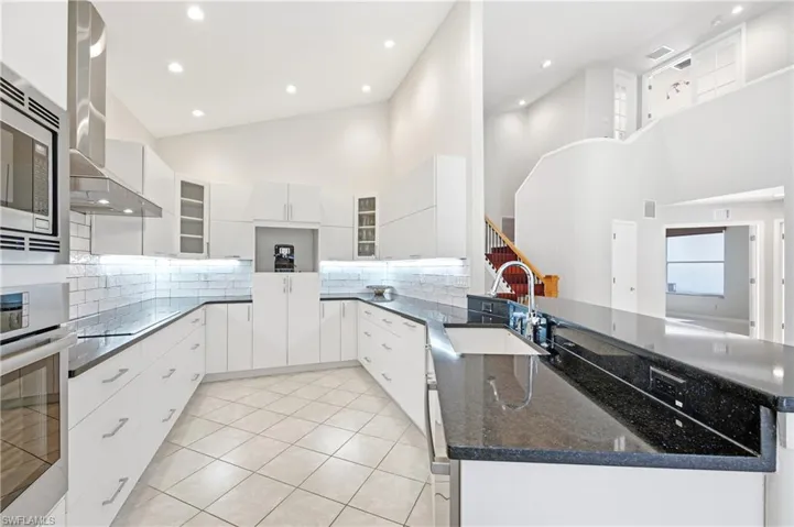 U-shaped kitchen featuring white cabinetry, dark countertops, a built-in stainless steel microwave, and an integrated sink with a gooseneck faucet