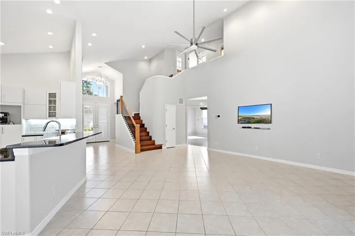 Spacious open-concept living area featuring high vaulted ceilings, large format tile flooring, a contemporary ceiling fan, and a prominent kitchen island with a dark countertop