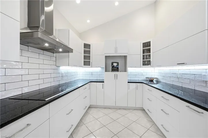 Bright kitchen featuring vaulted ceilings, white cabinetry, dark countertops, white subway tile backsplash, and under-cabinet lighting