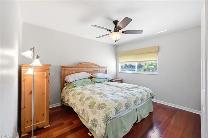 Bedroom 4 featuring wood-finish flooring, a ceiling fan with integrated lighting, a window with a roller shade, and white baseboards