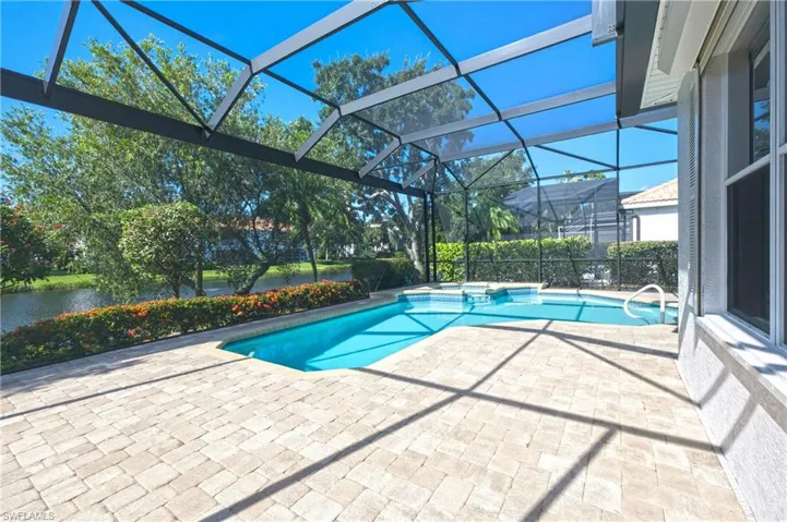 Screened lanai featuring a swimming pool and attached spa, paver deck, and waterfront landscaping
