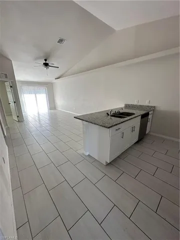 Kitchen featuring white cabinetry, dark stone countertops, a peninsula, ceiling fan, and lofted ceiling