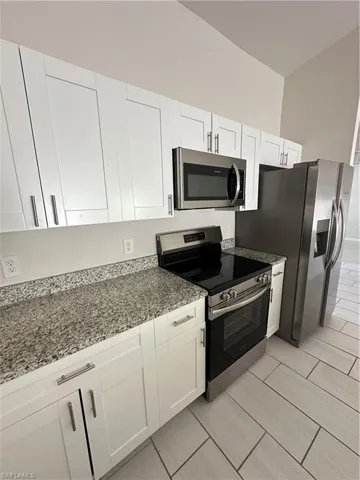 Kitchen featuring range, stainless steel microwave, white cabinetry, and light stone counters
