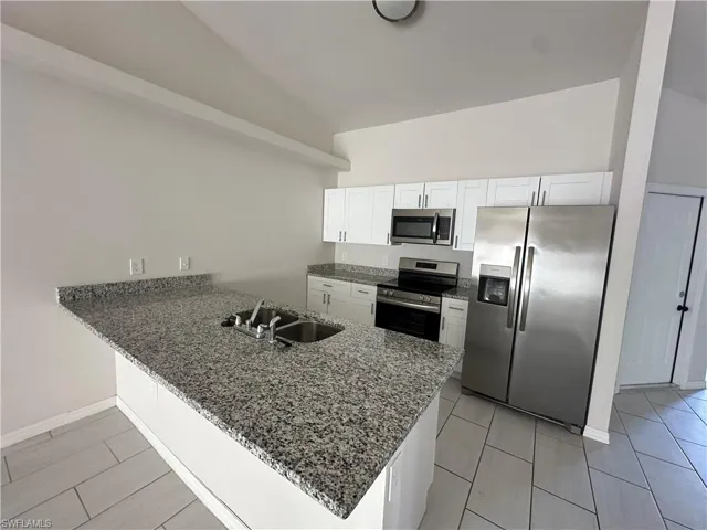 Kitchen with stainless steel appliances, dark stone counters, a peninsula, lofted ceiling, and white cabinets
