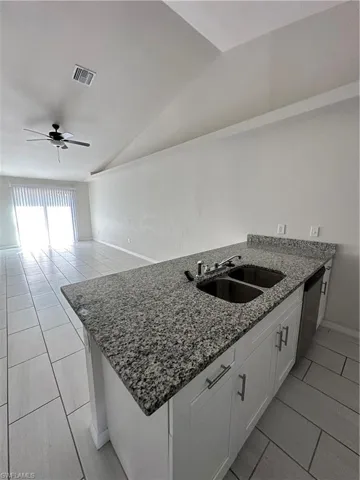 Kitchen with a peninsula, light stone countertops, ceiling fan, white cabinets, and light tile patterned floors