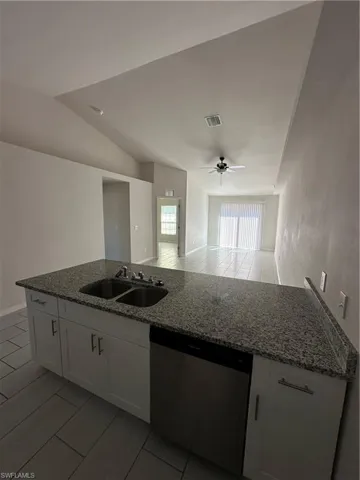 Kitchen featuring dark stone counters, white cabinets, a ceiling fan, dishwasher, and lofted ceiling