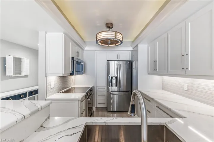 Kitchen featuring appliances with stainless steel finishes, white cabinetry, tasteful backsplash, and light stone counters