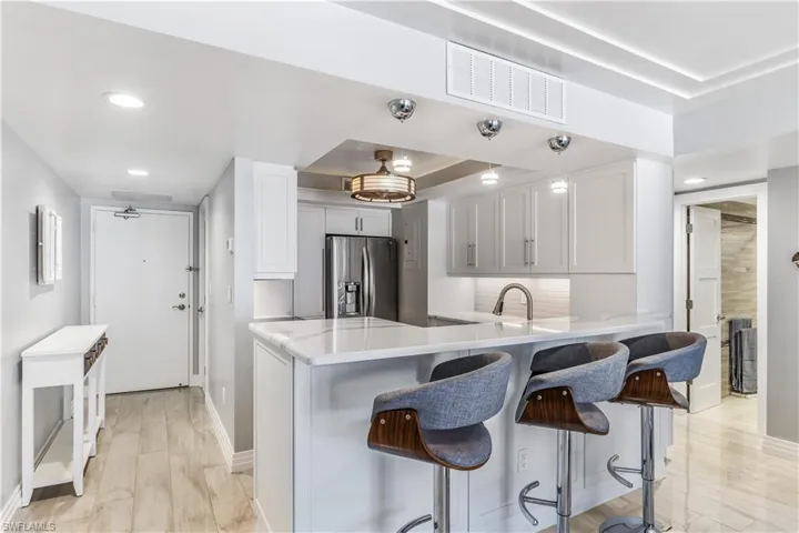 Kitchen with stainless steel refrigerator with ice dispenser, a raised ceiling, a peninsula, a kitchen breakfast bar, and recessed lighting