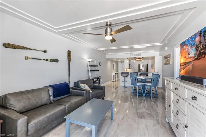 Living room with a ceiling fan, a raised ceiling, and light wood finished floors