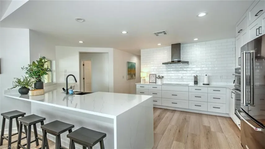 Kitchen with wall chimney range hood, light stone counters, decorative backsplash, high end refrigerator, and a breakfast bar