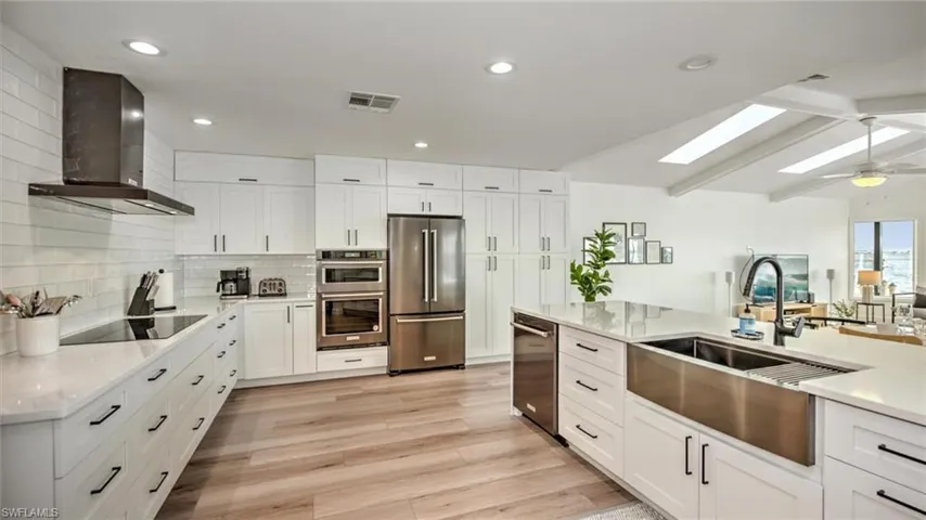 Kitchen featuring stainless steel appliances, wall chimney exhaust hood, a skylight, decorative backsplash, and light countertops