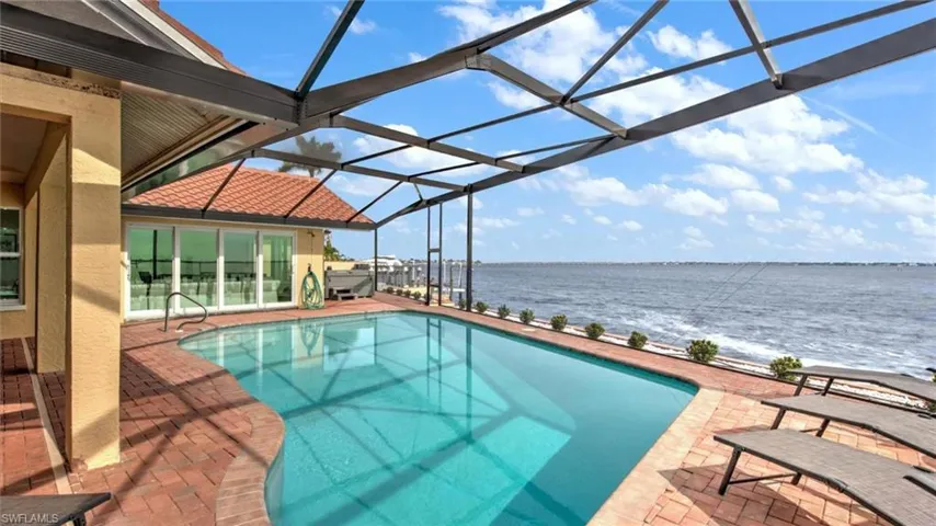 Outdoor pool with a water view, a patio area, and glass enclosure