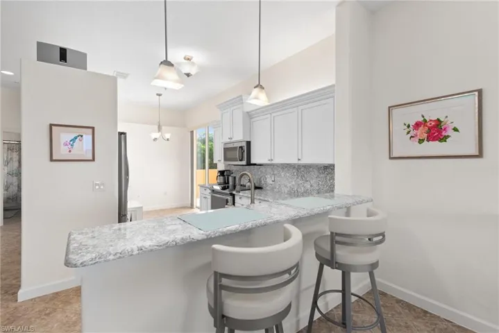 Kitchen with white cabinets, stainless steel appliances, kitchen peninsula, backsplash, and light tile patterned floors