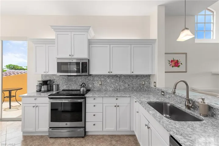 Kitchen with light tile patterned flooring, backsplash, stainless steel appliances, hanging light fixtures, and sink