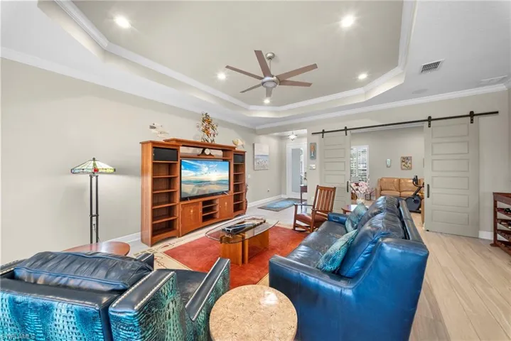 The spacious living area features a tray ceiling with recessed lighting and a ceiling fan, light-colored flooring, and dual barn doors