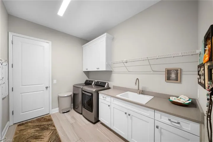 Laundry room featuring light-colored flooring, white cabinetry, a sink with a faucet, and a countertop