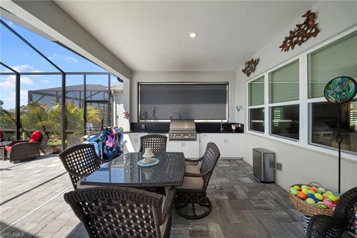 This screened lanai features an outdoor kitchen with a built-in grill and cabinetry, a dining area with a table and chairs, and a spacious tiled floor