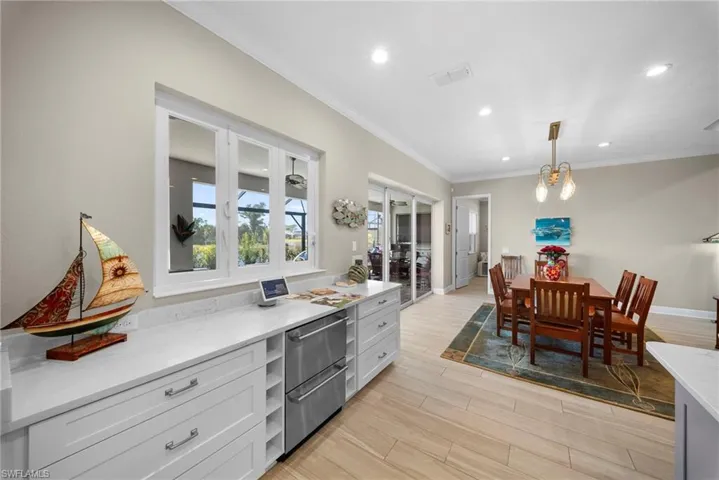 This open-concept area features white cabinetry with stone countertops, a large window, and light wood flooring