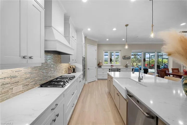 Modern kitchen featuring white cabinetry, light-colored countertops, a gas range with a decorative hood, and a large kitchen island with an integrated sink