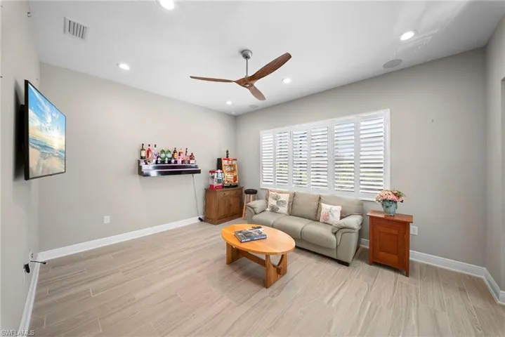 This living area features a modern ceiling fan, recessed lighting, and large windows with plantation shutters